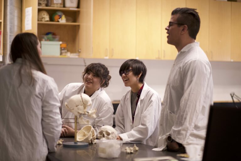 Four Indigenous students from the Haida, Metis and Ntekepmx Nations gathered around a table with a skull prop on it in a biology laboratory.