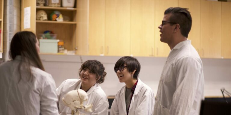 Four Indigenous students from the Haida, Metis and Ntekepmx Nations gathered around a table with a skull prop on it in a biology laboratory.